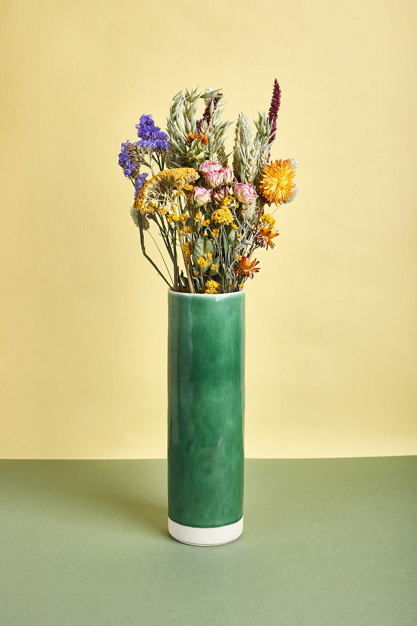 Green vase with colorful flowers on a green and beige background