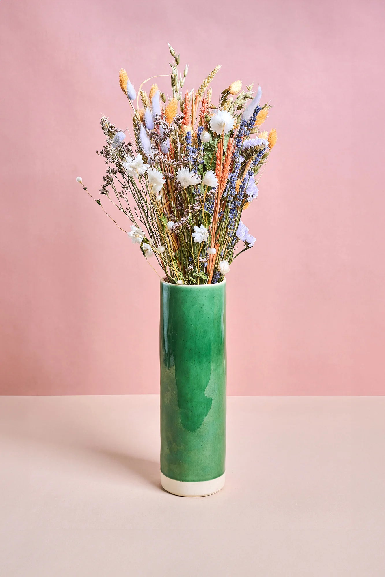 Green vase with dried flowers against a pink background