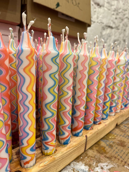 Row of colorful wavy-patterned candles on a wooden board.
