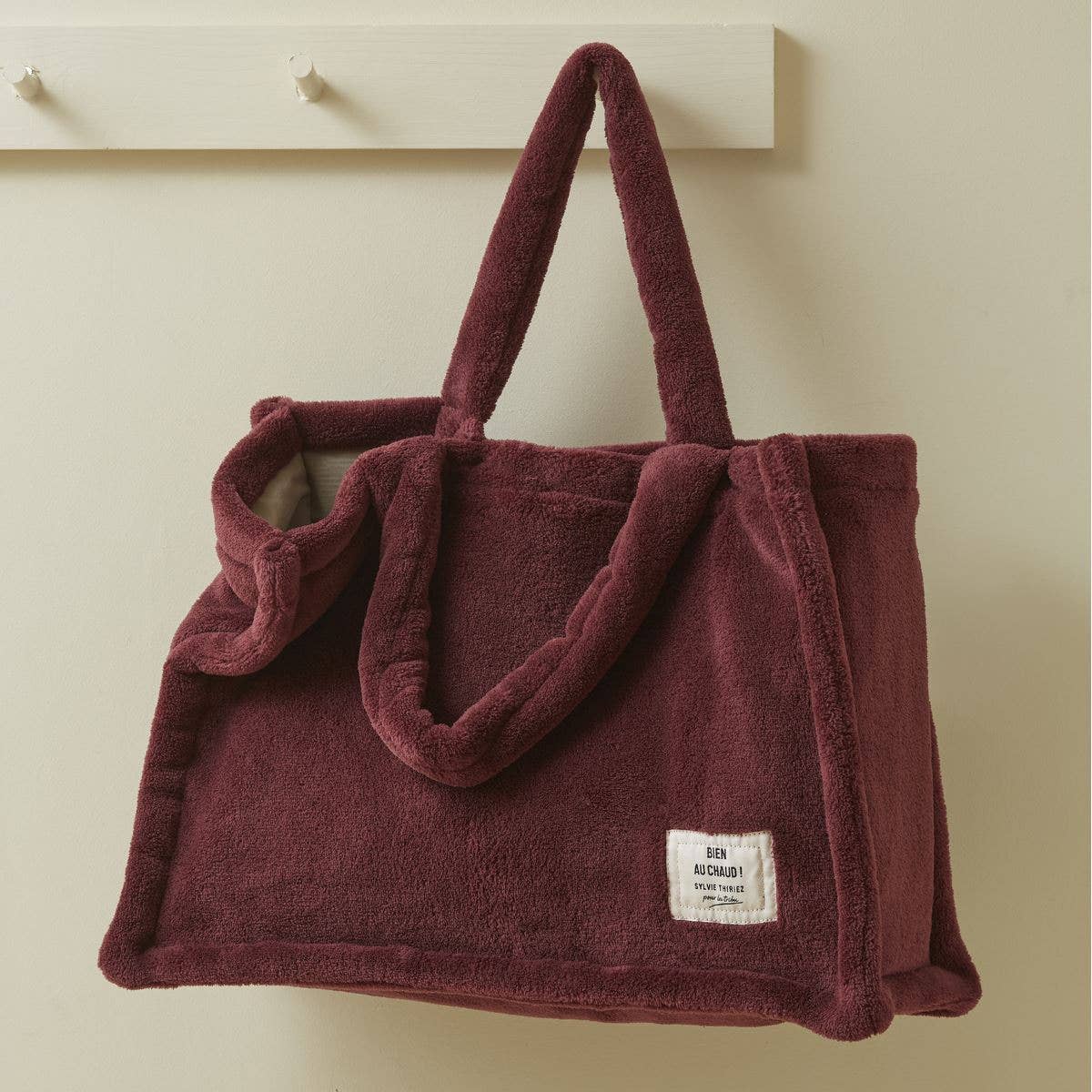 Maroon plush bag with a visible brand label on a beige background