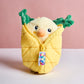 Plush toy resembling a bird wrapped in yellow fabric with green leaves on a pink background