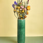 Green vase with colorful flowers on a green and beige background