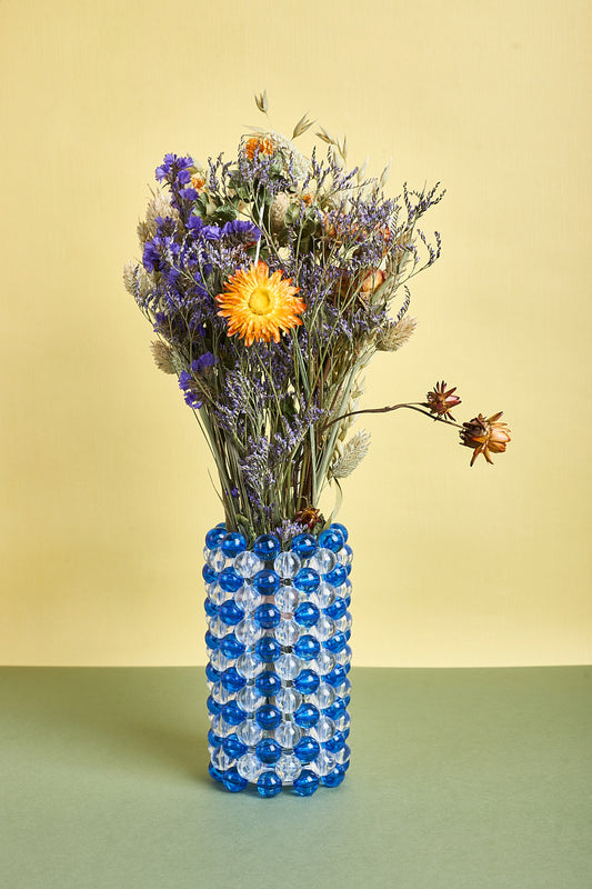 Blue beaded vase with a bouquet of flowers on a green surface and yellow background