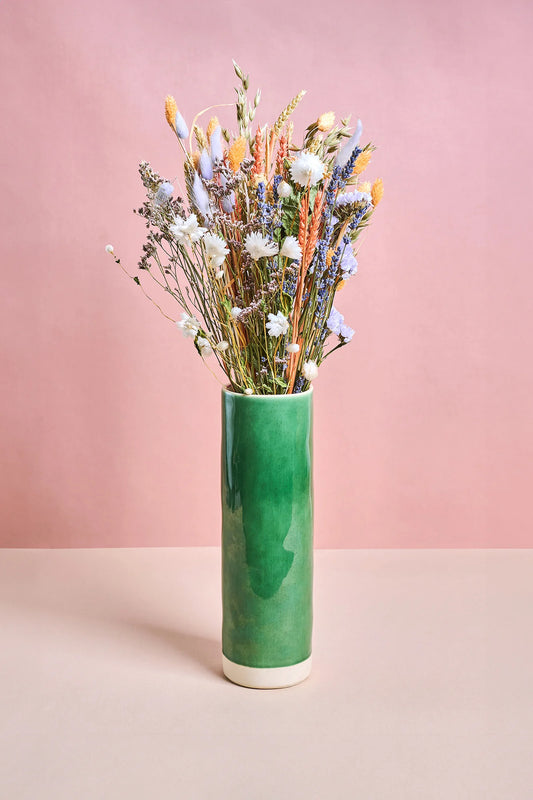 Green vase with dried flowers against a pink background